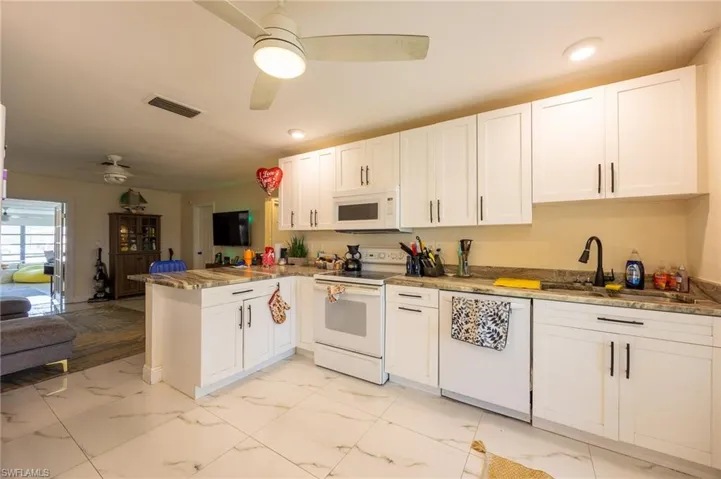 Kitchen featuring marble finish floor, visible vents, a sink, white appliances, and a peninsula