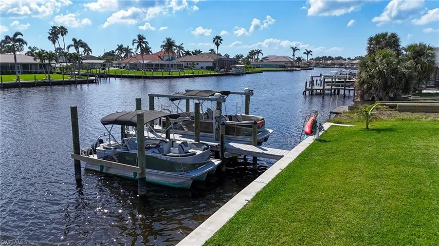 View of dock with a lawn, a water view, boat lift, and a residential view