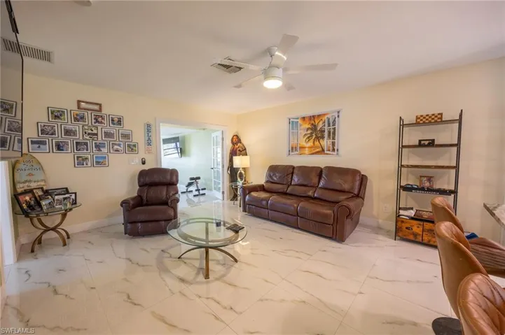 Living area with a ceiling fan, marble finish floor, visible vents, and baseboards