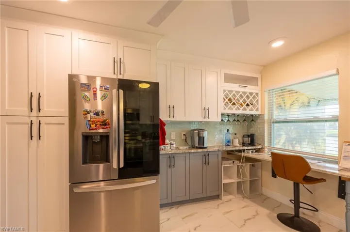 Kitchen with stainless steel fridge, decorative backsplash, light stone countertops, marble finish floor, and white cabinetry