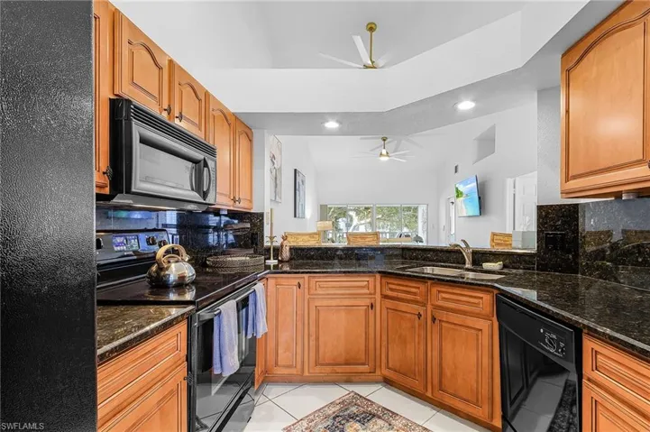 Kitchen featuring decorative backsplash, black appliances, dark stone counters, light tile patterned flooring, and recessed lighting