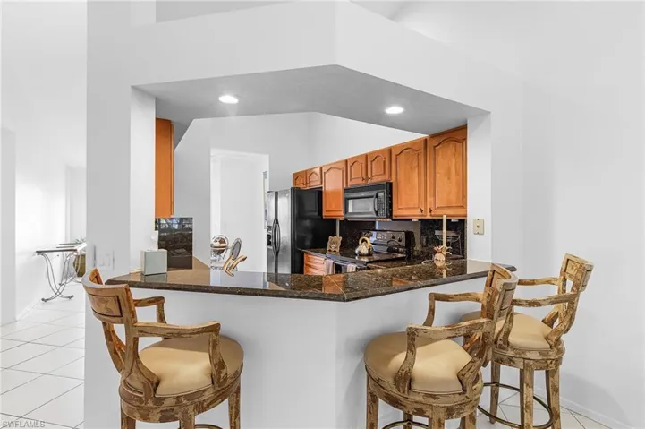 Kitchen with light tile patterned floors, backsplash, black appliances, a breakfast bar, and recessed lighting