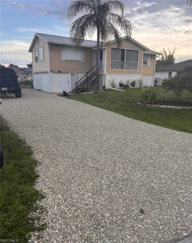 Elevated home featuring a metal roof, screened porch, exterior staircase, and a large gravel driveway