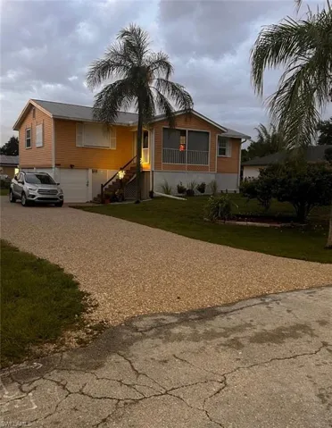 residence featuring a Yellow exterior, a gravel driveway, mature palm trees, a screened-in porch, and a two-car garage