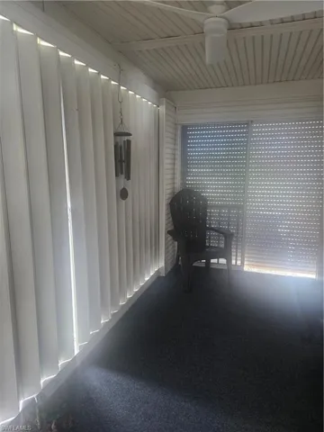 Screened porch with shutters featuring a textured ceiling, a ceiling fan, vertical blinds, and dark grey carpeting