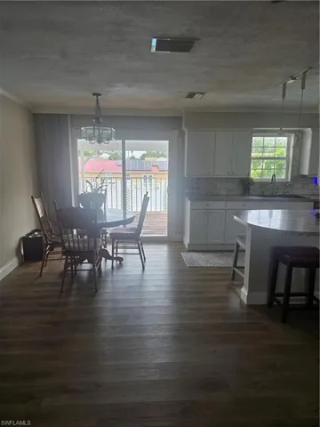 Open-concept living space featuring wood-finish flooring, white kitchen cabinetry, a kitchen island with seating, and sliding glass doors opening to an outdoor deck