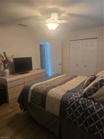 Spacious bedroom featuring wood-finish flooring, a ceiling fan with integrated lighting, and white bi-fold closet doors