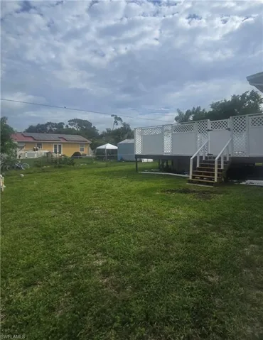 Expansive green lawn with a raised deck featuring white lattice railings and a stairway