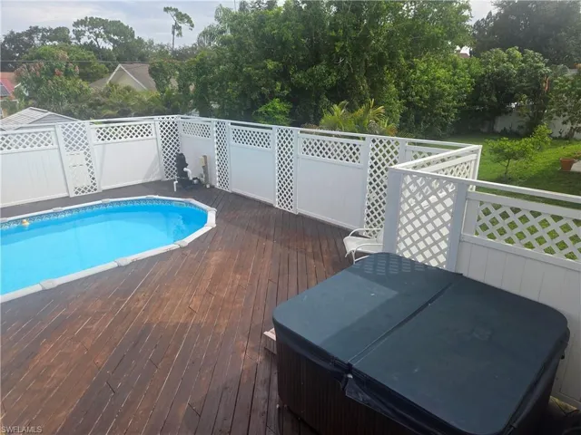 Expansive wood-finish deck featuring an above-ground swimming pool, an adjacent hot tub, and white lattice fencing