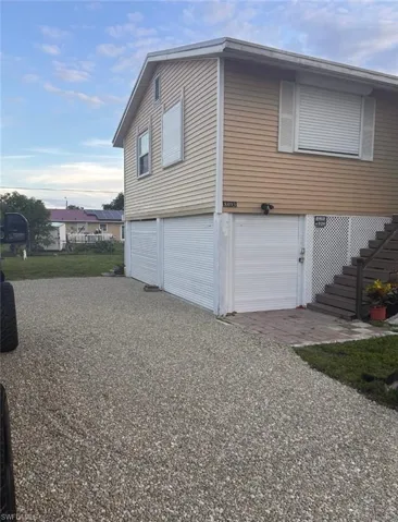 Elevated home featuring light yellow siding, multiple windows with white shutters, and a gravel driveway