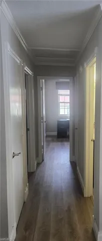 Hallway featuring wood-finish flooring, white trim, and a tray ceiling