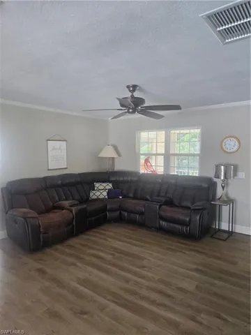 Spacious living area featuring wood-finish flooring, a ceiling fan, crown molding, and natural light from multiple windows