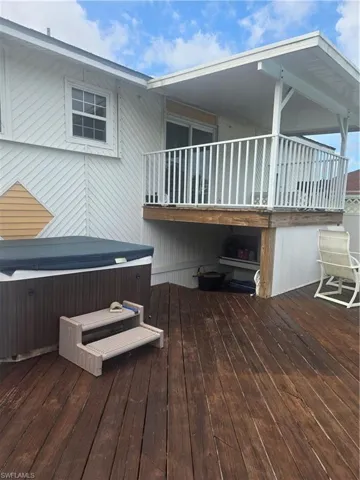 Spacious wood-finish deck featuring an integrated hot tub and an upper-level covered balcony with white railing and sliding glass door access