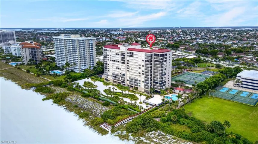 Multi-story residential building with private balconies, surrounded by mature landscaping, a swimming pool, and hardscaped recreational areas