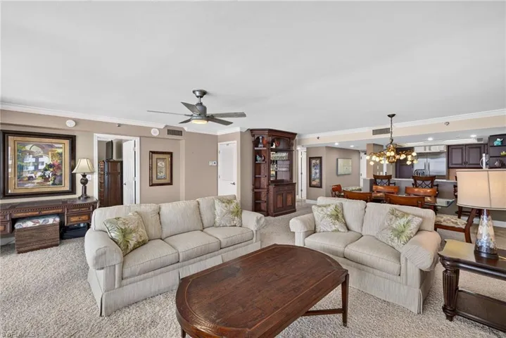 Open-concept living area featuring neutral-toned walls, crown molding, and a ceiling fan