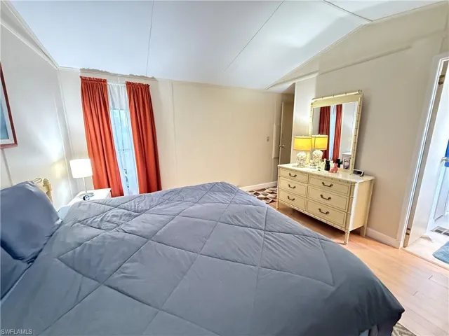 Bedroom featuring a decorative wall, light wood-style floors, and lofted ceiling
