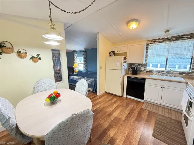 Kitchen with decorative backsplash, white appliances, hanging light fixtures, light countertops, and white cabinetry