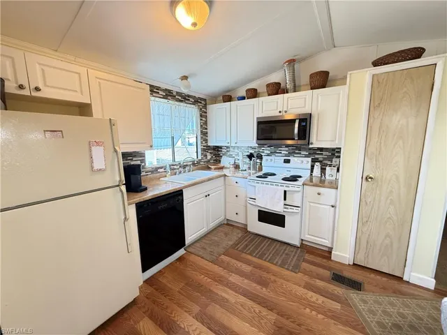 Kitchen with white appliances, light countertops, white cabinetry, dark wood finished floors, and tasteful backsplash