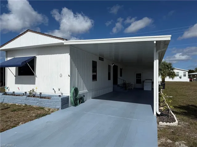 View of front facade with an attached carport, driveway, a front yard, entry steps, and a patio area