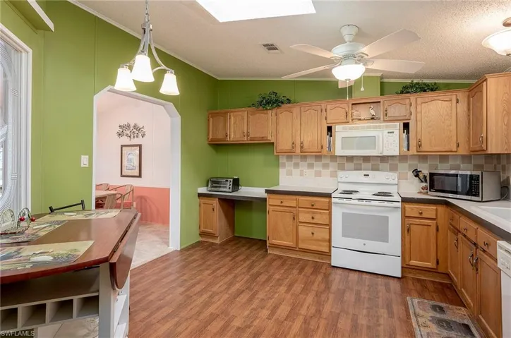 Kitchen featuring ornamental molding, white appliances, a textured ceiling, dark wood-type flooring, and hanging light fixtures