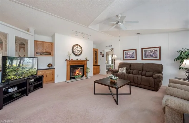 Carpeted living room with a textured ceiling, ceiling fan, rail lighting, and vaulted ceiling