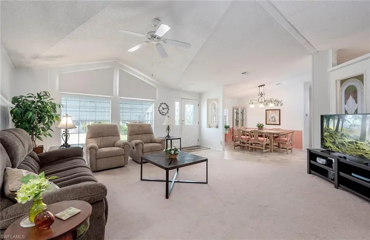 Carpeted living room featuring ceiling fan with notable chandelier, a textured ceiling, and vaulted ceiling