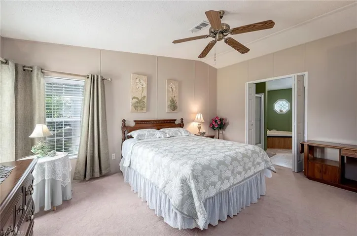 Bedroom featuring a textured ceiling, connected bathroom, light colored carpet, and ceiling fan