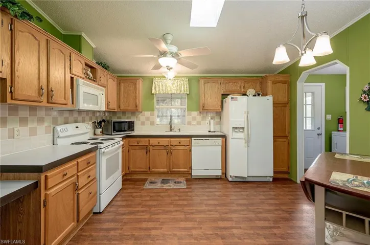 Kitchen with dark hardwood / wood-style floors, crown molding, pendant lighting, white appliances, and ceiling fan with notable chandelier