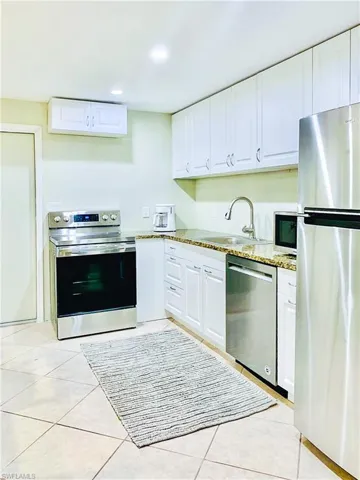Kitchen featuring stainless steel appliances, white cabinets, light stone countertops, light tile patterned flooring, and recessed lighting