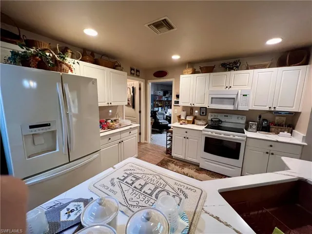 Kitchen with white cabinetry, white appliances, and light wood-type flooring