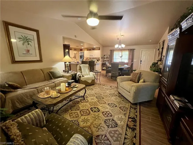 Living room with hardwood / wood-style floors, ceiling fan with notable chandelier, and vaulted ceiling
