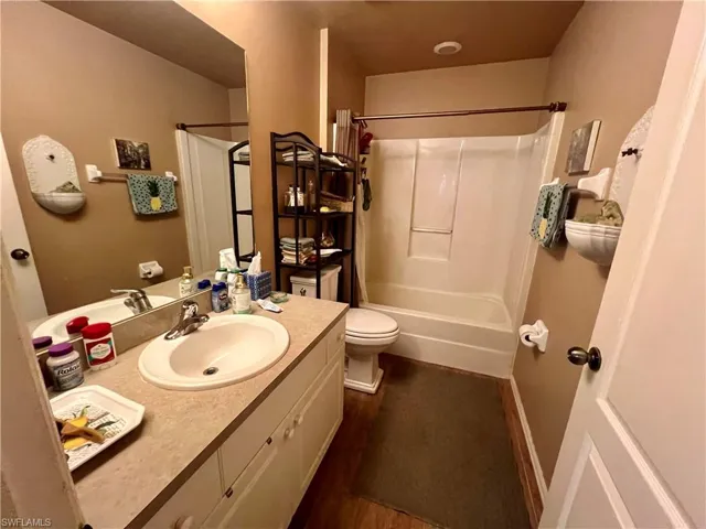Full bathroom featuring wood-type flooring, shower / bathtub combination with curtain, vanity, and toilet