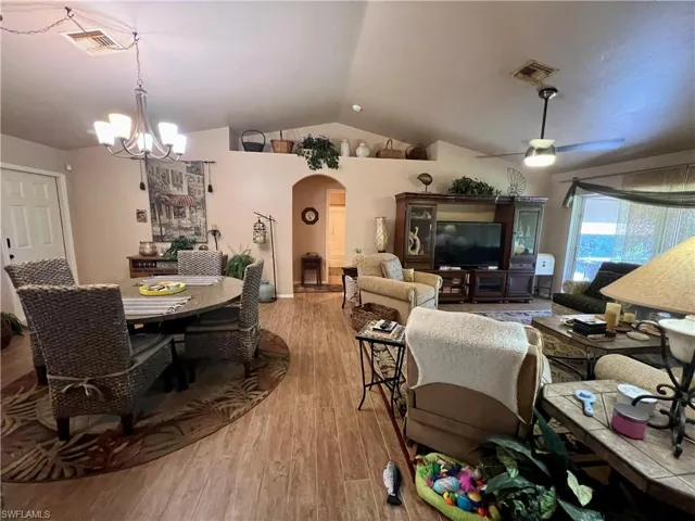 Living room featuring light hardwood / wood-style floors, ceiling fan with notable chandelier, and vaulted ceiling