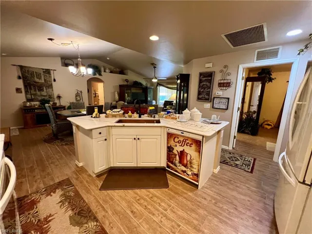 Kitchen featuring white appliances, light wood-type flooring, white cabinets, ceiling fan with notable chandelier, and sink