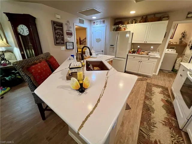 Kitchen with white cabinets, sink, washer / clothes dryer, white refrigerator with ice dispenser, and wood-type flooring