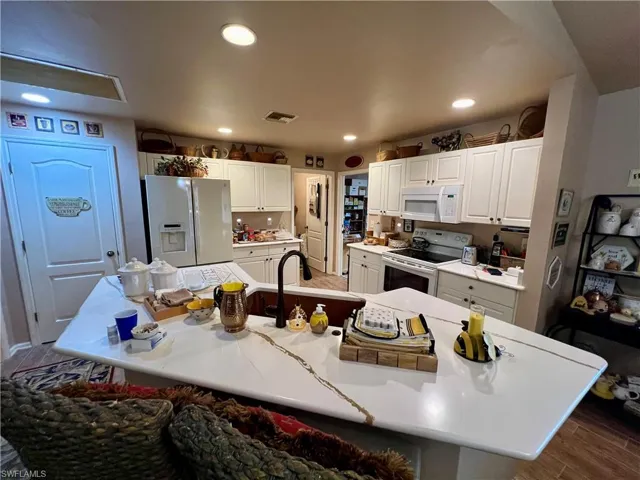 Kitchen with hardwood / wood-style flooring, white cabinets, an island with sink, white appliances, and sink