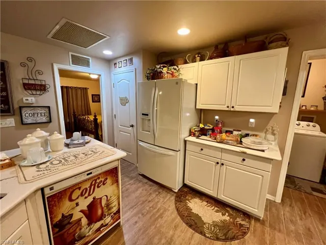 Kitchen with white cabinetry, washer / dryer, white fridge with ice dispenser, and light wood-type flooring