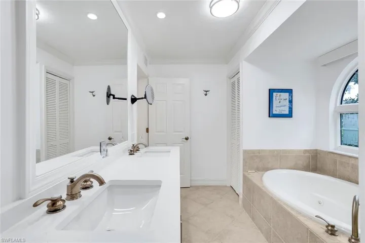 Bathroom with a closet, a bath, double vanity, light tile patterned floors, and ornamental molding