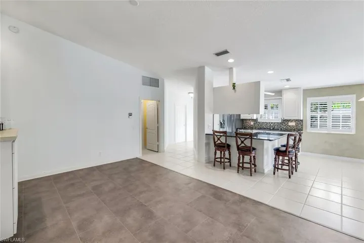 Kitchen with a breakfast bar, white cabinets, backsplash, stainless steel refrigerator with ice dispenser, and light tile patterned floors