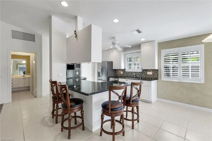 Kitchen with dark stone countertops, a peninsula, a kitchen bar, tasteful backsplash, and white cabinetry