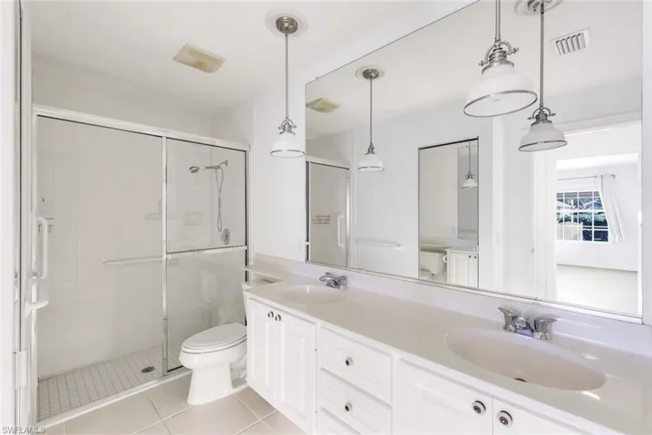 Bathroom featuring double vanity, a stall shower, and light tile patterned floors