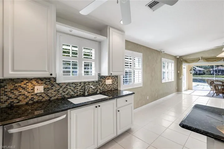 Kitchen featuring ceiling fan, dark stone countertops, dishwasher, white cabinets, and vaulted ceiling