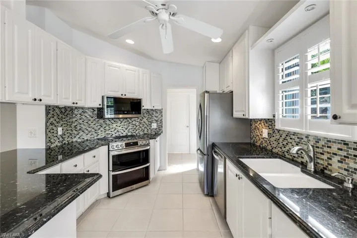 Kitchen featuring dark stone countertops, white cabinets, stainless steel appliances, a ceiling fan, and light tile patterned floors