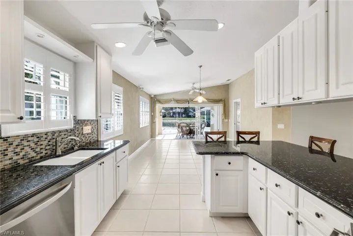 Kitchen featuring lofted ceiling, dark stone countertops, a breakfast bar, dishwasher, and white cabinetry