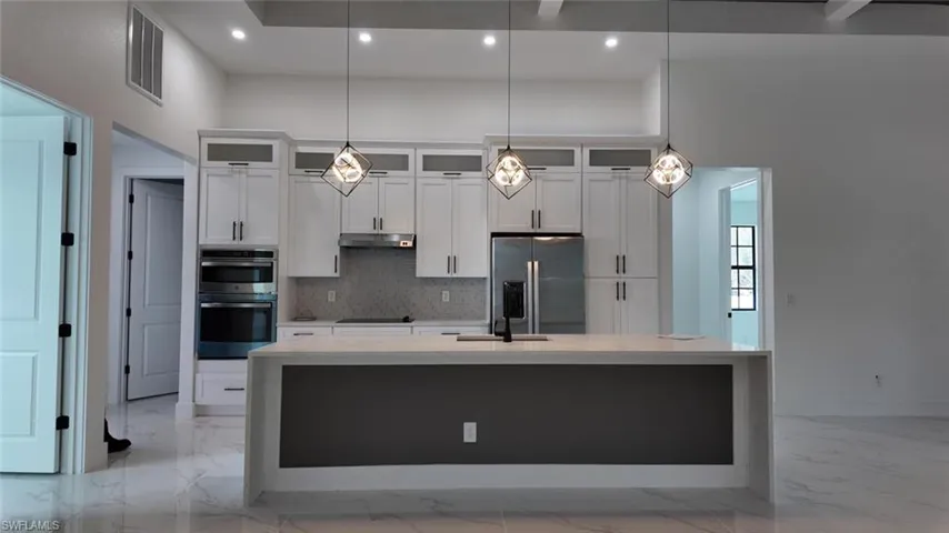 Kitchen with a center island with sink, stainless steel appliances, tasteful backsplash, hanging light fixtures, and white cabinets