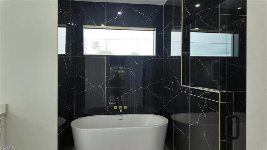 Bathroom featuring tile walls, vanity, and shower with separate bathtub