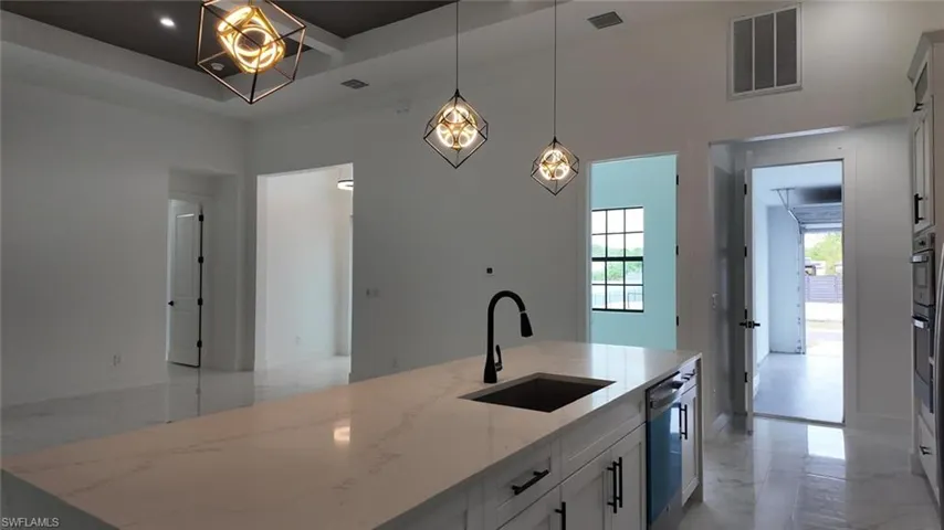 Kitchen with light stone countertops, sink, white cabinetry, and a center island with sink