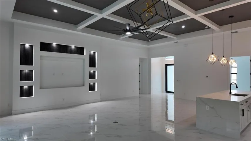 Unfurnished living room featuring ceiling fan, a towering ceiling, sink, beamed ceiling, and coffered ceiling