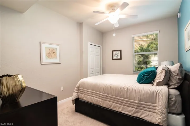 Carpeted guest bedroom featuring a ceiling fan with integrated lighting, a window with horizontal blinds, and a built-in closet with a bi-fold door