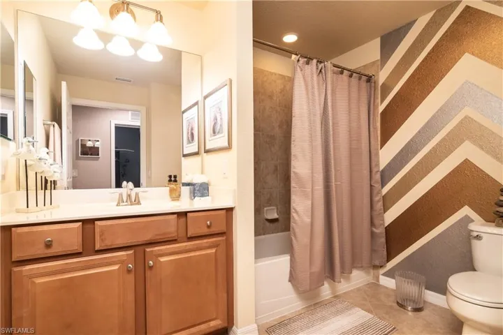 Full guest bathroom featuring a single vanity with wood cabinetry, a large mirror, and a shower-tub combination with a tiled surround